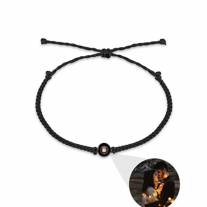A black braided cord bracelet with a central circular charm containing a small pink stone, displayed on a white background with a circular inset photo of a couple at night.