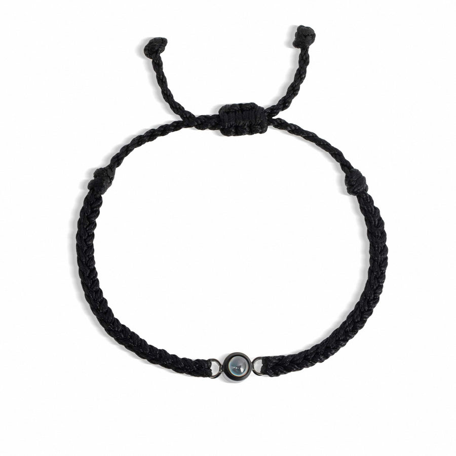 Black braided bracelet with a small round bead on a white background