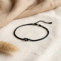 Black Love Knot Bracelet with lobster clasp and adjustable extender chain on cream linen