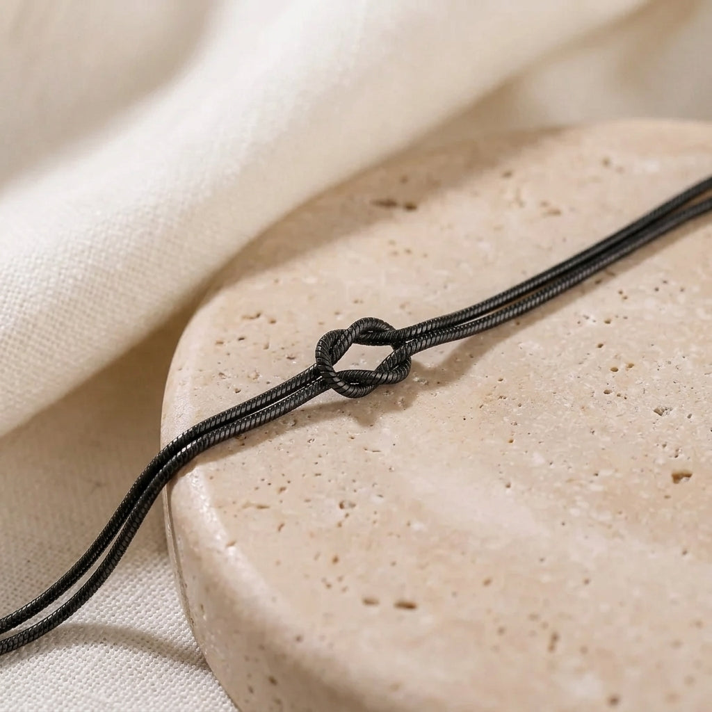 Black Love Knot Bracelet close-up on a travertine stone, showing the double snake chain and knot