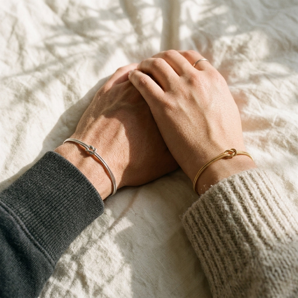 Two hands resting together on linen in sunlight, wearing matching silver and gold Love Knot Bracelets