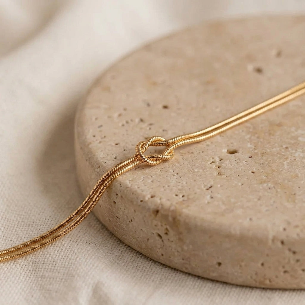 Gold Love Knot Bracelet close-up on a round travertine stone, showing the double snake chain and knot