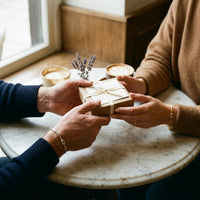 Couple exchanging a gift box over coffee, wearing matching gold and silver Love Knot Bracelets