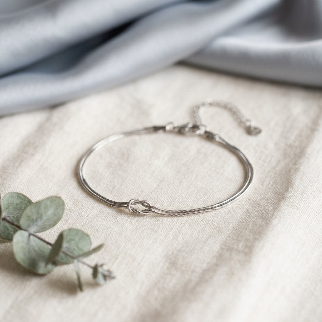 Silver Love Knot Bracelet with lobster clasp and adjustable extender chain on cream linen beside eucalyptus