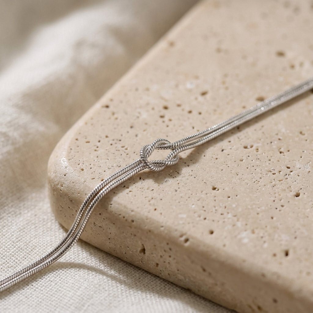 Silver Love Knot Bracelet close-up on a travertine stone, showing the double snake chain and knot