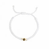 A delicate white braided cord bracelet with an adjustable sliding knot and a central gold-toned charm featuring a dark oval stone, shown on a plain white background.
