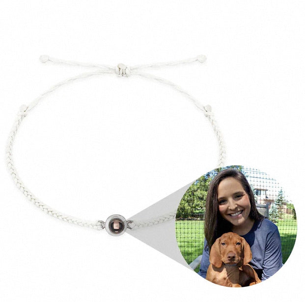 A white braided cord bracelet with a silver-toned circular charm holding a small photo of a per and a girl , shown on a plain white background with an inset demonstrating the photo insertion.