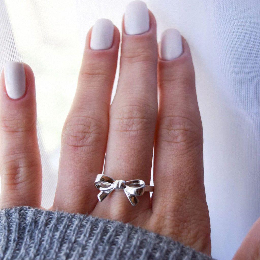 delicate silver bow ring on finger near window light