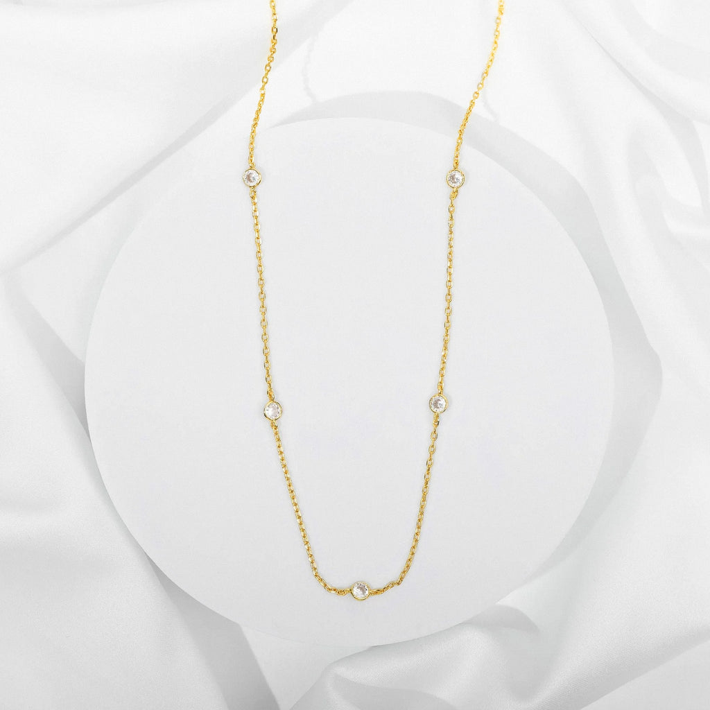 Gold station necklace with bezel-set cubic zirconia stones on white background