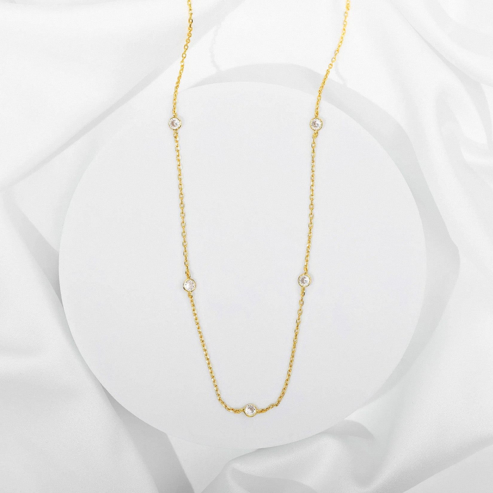Gold station necklace with bezel-set cubic zirconia stones on white background