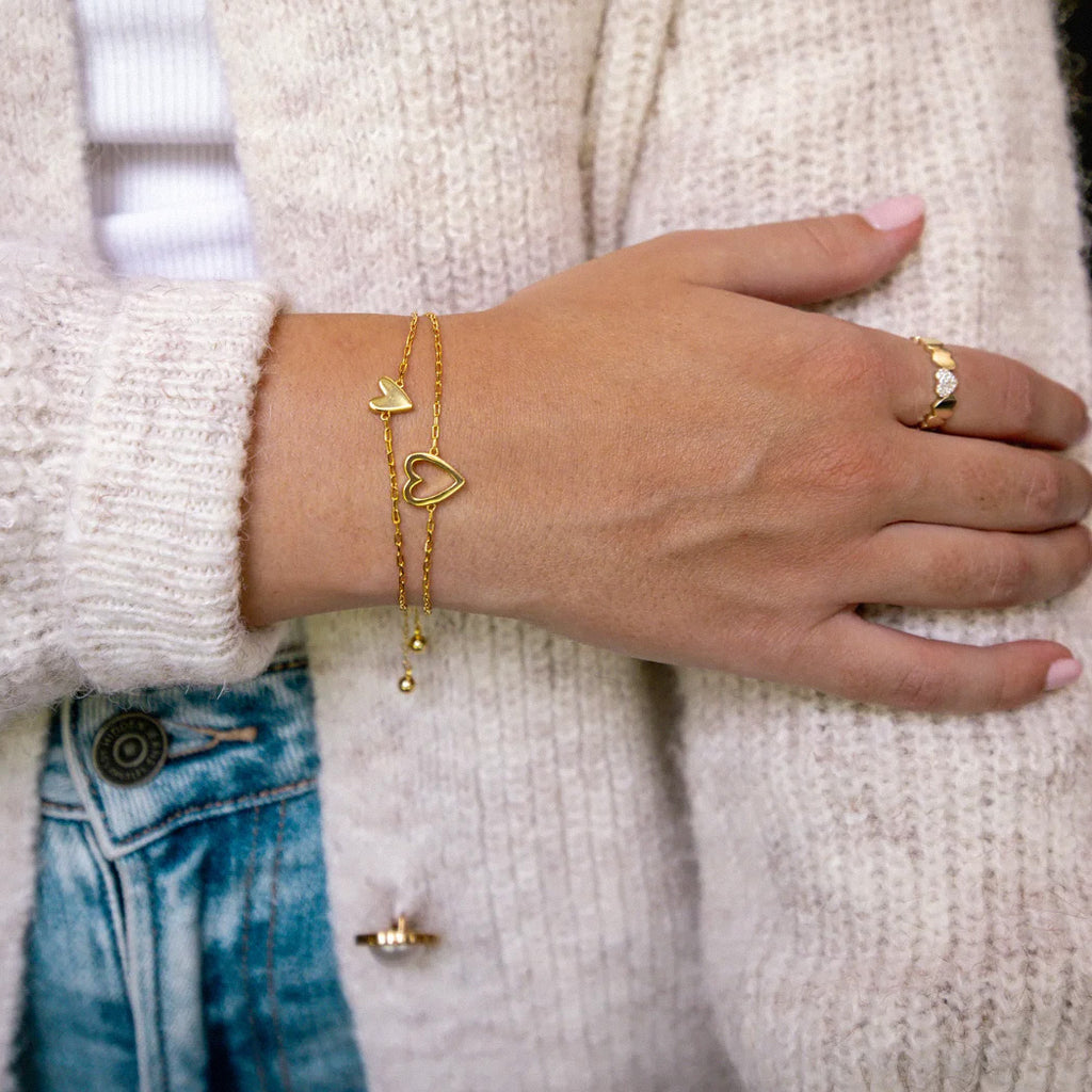 Layered gold heart charm bracelets styled with casual outfit