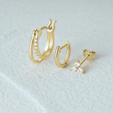 Gold hoop earrings and stud earrings on a light gray background