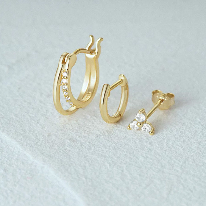 Gold hoop earrings and stud earrings on a light gray background