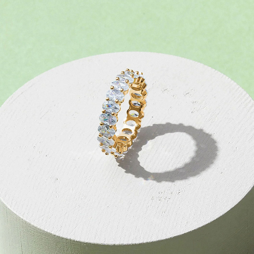 White gold-plated oval zirconia eternity ring displayed on minimal pedestal