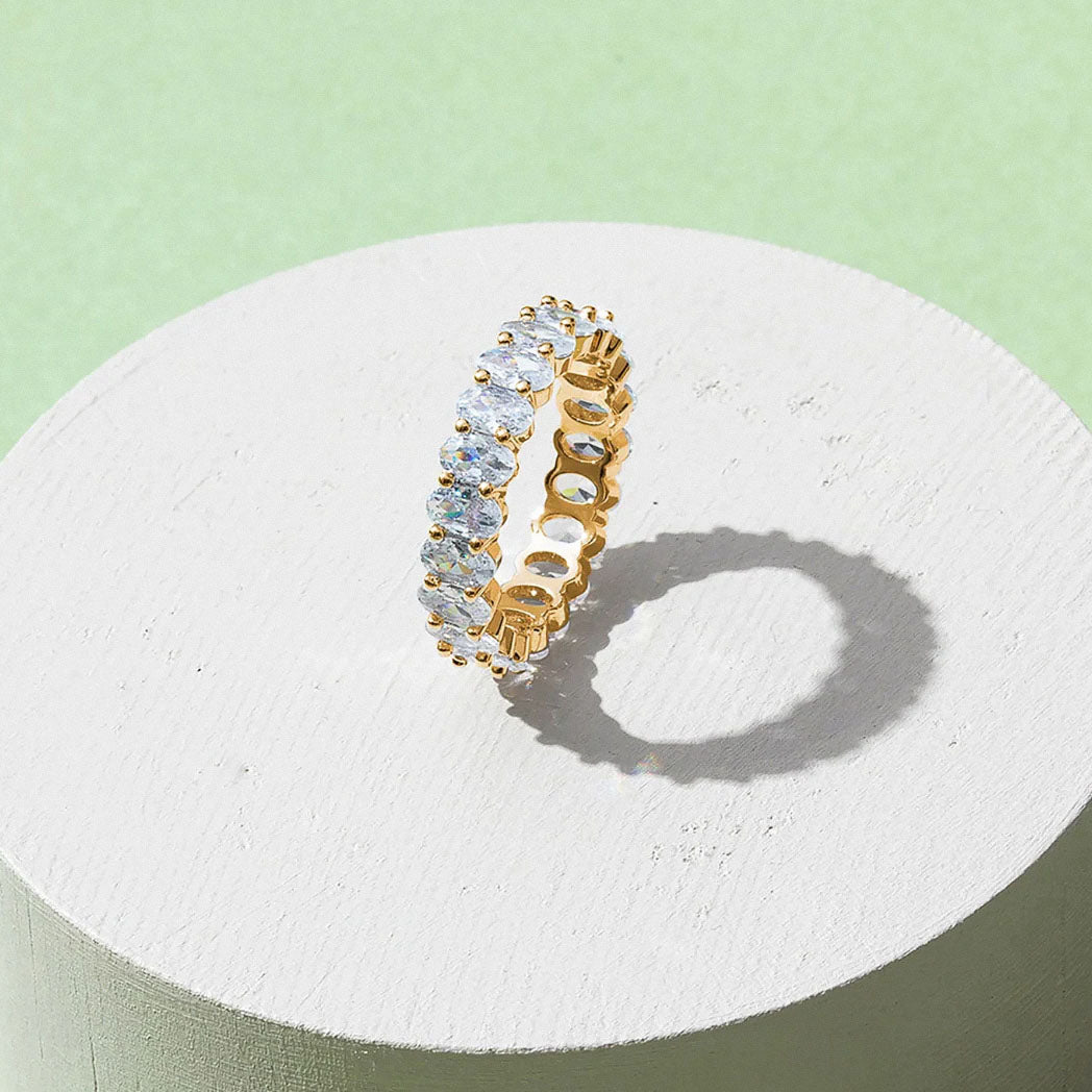 White gold-plated oval zirconia eternity ring displayed on minimal pedestal
