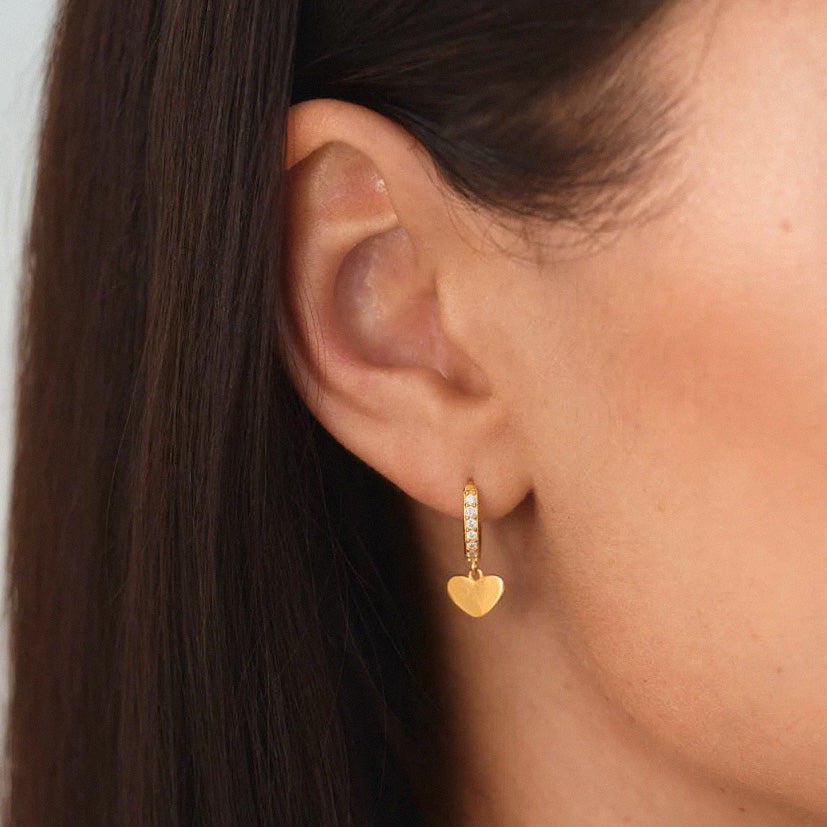 Woman wearing gold heart dangle huggie earrings close-up