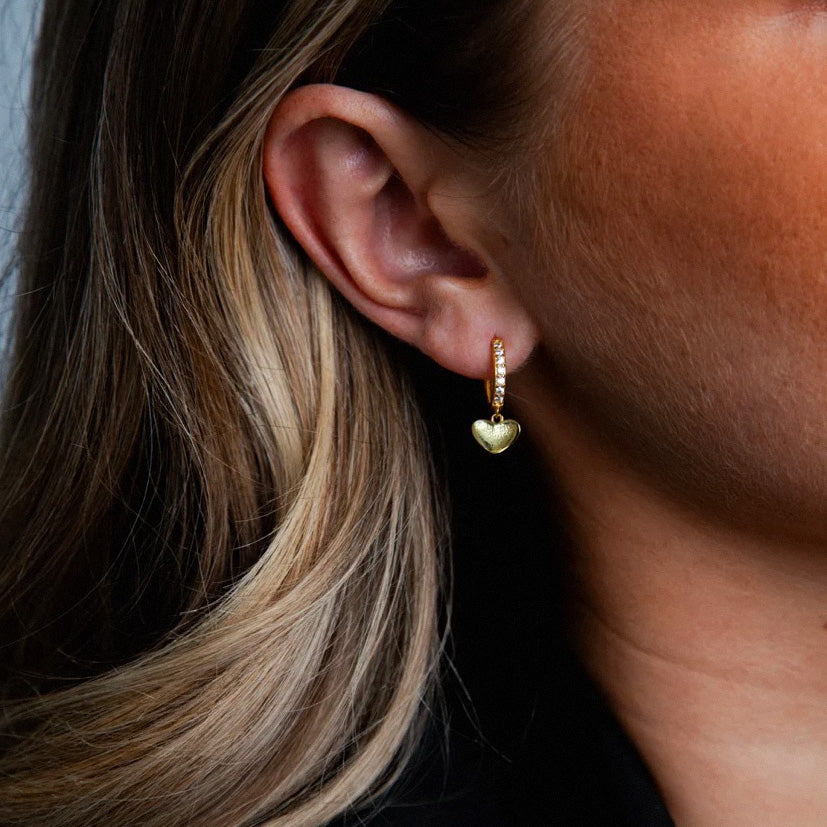 Female model showcasing minimalist gold heart dangle earrings