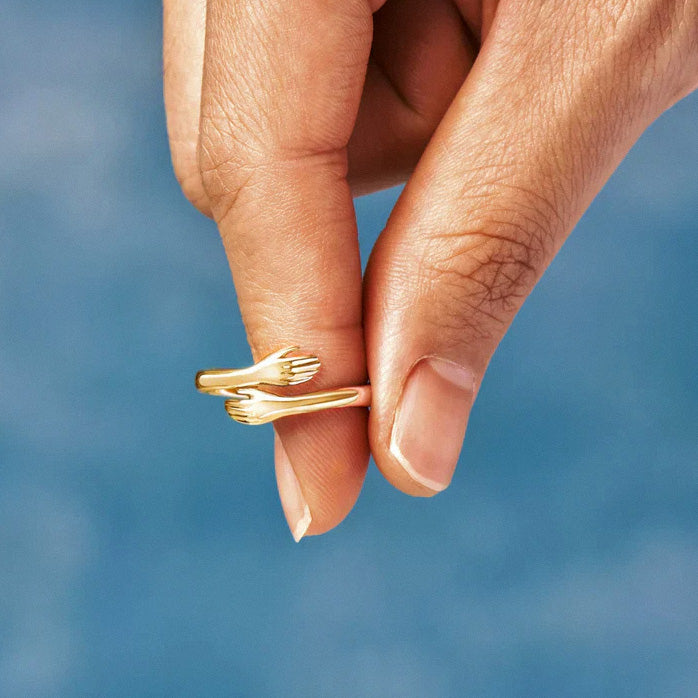 Gold hug ring with hand-shaped open band held between fingers