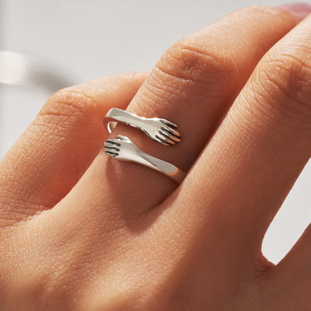Adjustable silver hug ring with sculpted hands worn on finger