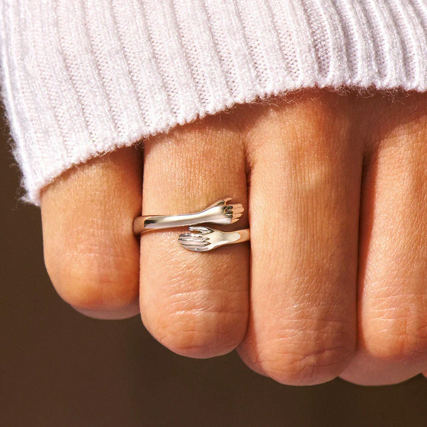 Silver hug ring with hand-shaped ends worn on finger