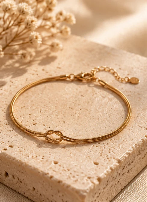 Gold Love Knot Bracelet with adjustable extender chain on a travertine stone