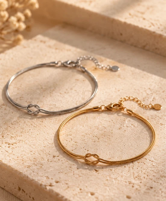 Silver and gold Love Knot Bracelets side by side on travertine stone