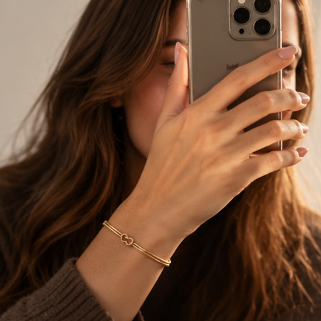 Woman taking a mirror photo, wearing a gold Love Knot Bracelet