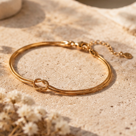 Gold Love Knot Bracelet resting on a stone with dried flowers