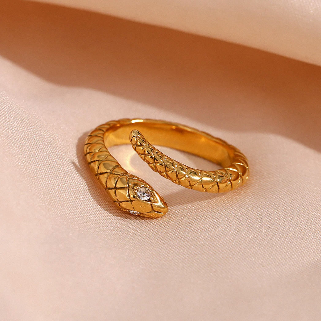 Gold textured snake ring with crystal detail on fabric background