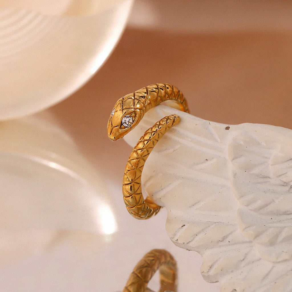 Gold textured snake ring positioned on white sculpted display