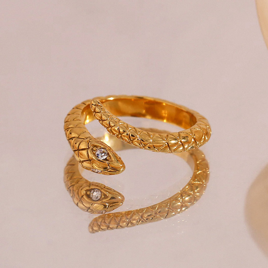 Gold snake ring with crystal detail displayed on reflective mirror surface