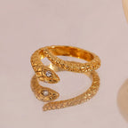Gold snake ring with crystal detail displayed on reflective mirror surface