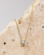 Aesthetic flat-lay of gold solitaire pendant necklace on stone background