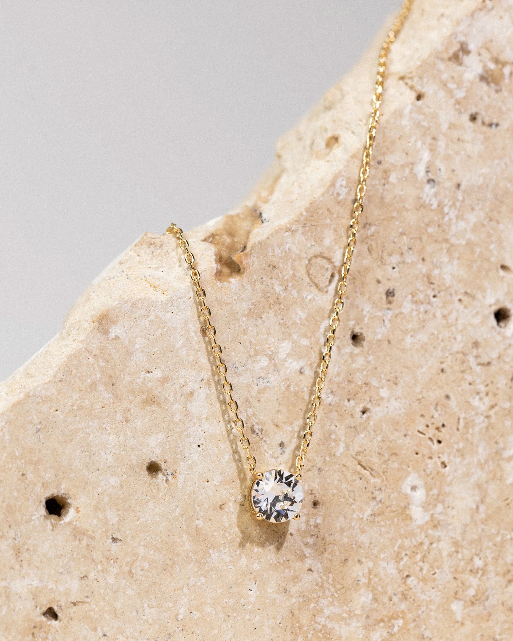 Aesthetic flat-lay of gold solitaire pendant necklace on stone background