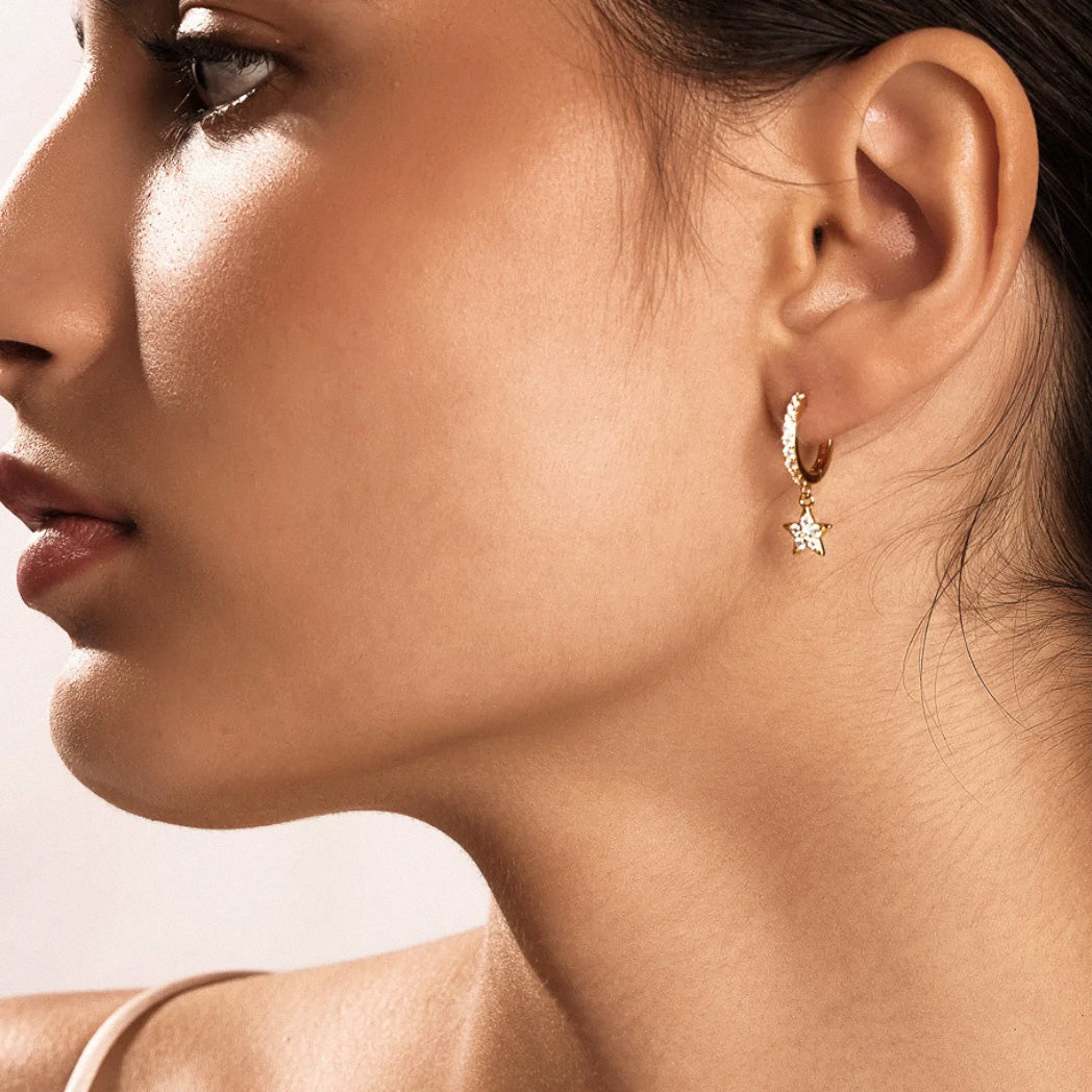 Gold star charm earrings styled on model with soft makeup