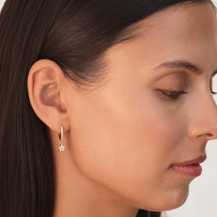 Gold star drop huggie earrings worn on model