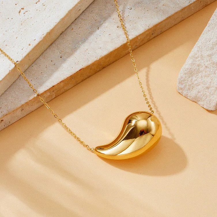 Gold polished teardrop pendant necklace on beige surface